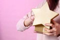 Gift box in the shape of a gold star in the hands of a young Asian girl. on a pink isolated background