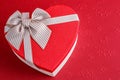 Gift box in the shape of a heart with a ribbon on a red background. The concept is suitable for love stories, birthdays and Valent