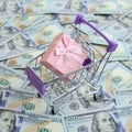 Gift box in a small shopping cart lies on a many dollar bills Royalty Free Stock Photo
