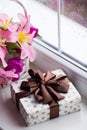 Gift box and tender bouquet of beautiful pink tulips in white basket near window with raindrops in the daylight Royalty Free Stock Photo