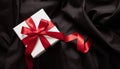 Gift box white with red ribbon on black satin. Christmas Valentine day present, black Friday Royalty Free Stock Photo