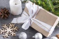 Gift box with white ribbon and rope, silver balls, spruce branch, candle, cone, snowflake, gray background