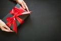 Gift box wrapped in black paper with red ribbon in female hand on black surface. Royalty Free Stock Photo