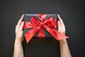 Gift box wrapped in black paper with red ribbon in female hand on black surface. Royalty Free Stock Photo