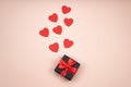 Gift box wrapped in black paper with red ribbon in female hand on pink surface. Flying red hearts symbol of love. Royalty Free Stock Photo