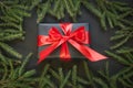 Gift box wrapped in black paper with red ribbon in female hand on black surface. Top view. Christmas card. Royalty Free Stock Photo