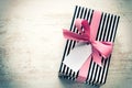 Gift box wrapped in black and white striped paper with pink ribbon on a white wood old background. Empty note tied over. Vintage Royalty Free Stock Photo