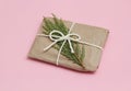 Gift box wrapped in brown craft paper and tie white string. Christmas mood. Solid pink background. Present package. Royalty Free Stock Photo