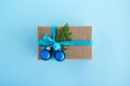 Gift box wrapped of craft paper, blue ribbon and decorated fir branches and blue Christmas balls on the blue background, top view. Royalty Free Stock Photo