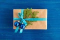 Gift box wrapped of craft paper, blue ribbon and decorated fir branches and blue Christmas balls on the blue wooden background. Royalty Free Stock Photo