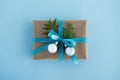 Gift box wrapped of craft paper, blue ribbon and decorated fir branches and silver Christmas balls on the blue background. Royalty Free Stock Photo