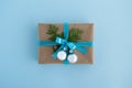 Gift box wrapped of craft paper, blue ribbon and decorated fir branches and silver Christmas balls on the blue background. Royalty Free Stock Photo