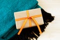 Gift box wrapped of craft paper and orange ribbon on a turquoise and black woolen plaid on the wooden background. Royalty Free Stock Photo