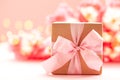 Gift box wrapped with craft paper and pink bow on pink flowers background