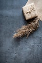 Gift box wrapped in craft paper with a reed stalk, dried pampas grass on a dark background. New fashionable home decor