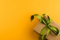 A gift box wrapped in craft paper and tied with a green ribbon on a yellow background close-up. Copy space Royalty Free Stock Photo