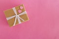 Gift box wrapped of craft paper and white ribbon with two pink hearts on the pink background. Royalty Free Stock Photo