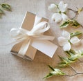 A gift box wrapped in festive silver with white bow and blank name tag with white spring flowers.  It`s square with top down view Royalty Free Stock Photo