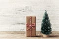 Gift box wrapped in kraft paper and little decorative fir tree on wooden rustic background. Christmas and New year concept.