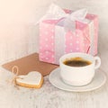 Gift box wrapped in pink dotted paper, heart shaped love cookie, a cup of coffee and an empty kraft card over a white wood Royalty Free Stock Photo