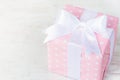 Gift box wrapped in pink dotted paper and tied satin bow over a white wood background.