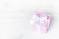 Gift box wrapped in pink dotted paper and tied satin bow over a white wood background.