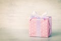 Gift box wrapped in pink dotted paper and tied satin bow over a white wood background. Vintage effect filter.