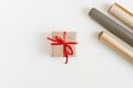 Gift box wrapped in polka dot kraft paper with red ribbon and paper rolls on white table Royalty Free Stock Photo