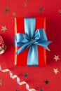 Gift box wrapped in re paper with blue ribbon on red surface. Christmas, party, birthday concept Royalty Free Stock Photo
