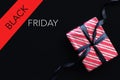 Gift box wrapped in red striped paper and tied with black bow on black background. Royalty Free Stock Photo