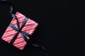 Gift box wrapped in red striped paper and tied with black bow on black background. Royalty Free Stock Photo
