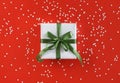 Gift box wrapped in white paper with green satin bow on festive red background with many snowflakes Royalty Free Stock Photo