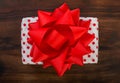 Gift box wrapped in white paper with red dots and bright red ribbon bow on a dark walnut wood. Background top view, close up Royalty Free Stock Photo