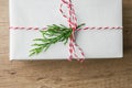 Gift box wrapped in white paper tied with striped red ribbon twig of green juniper on brown wood background. Christmas New Years Royalty Free Stock Photo