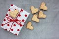 Gift box in wrapping paper with red polka dot pattern and heart shaped cookies on gray concrete background. Royalty Free Stock Photo