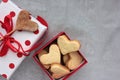 Gift box in wrapping paper with red polka dot pattern and heart shaped cookies on gray concrete background. Royalty Free Stock Photo