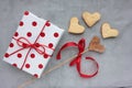 Gift box in wrapping paper with red polka dot pattern and heart shaped cookies on gray concrete background. Royalty Free Stock Photo