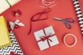 Gift boxes, paper, scisors, tape and christmas balls over red background