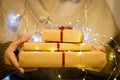 Gift boxes with red ribbon in the hands. Hands hold gifts in craft paper with luminous garland