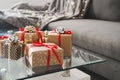 Gift boxes wrapped in craft paper on glass coffee table in the living room, sofa bed with blanket and decorative lights Royalty Free Stock Photo