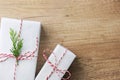 Gift boxes wrapped in white paper tied with striped red ribbon twig of green juniper on brown wood background. Christmas New Years
