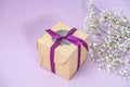 Gift craft box with ribbon on purple background with small white gypsophila flowers Royalty Free Stock Photo