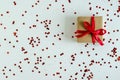 gift in craft packaging with a red satin ribbon on a white background with chaotically scattered red shiny sequins.