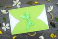 Gift envelope with green ribbon on floral wooden background. Congratulation with flowers. Flat lay