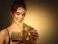 Gift giving for Woman. Beautiful Girl opening Present Box with shining Light. Happy smiling Model receive Surprise over Golden Royalty Free Stock Photo