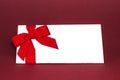 Gift isolated white card with red ribbon bow on deep red background. Royalty Free Stock Photo