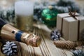 A gift lays on a wooden table next to a candle, cones and an angel against the background of Christmas decorations Royalty Free Stock Photo