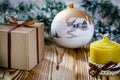 A gift lays on a wooden table next to a candle, cones and an angel against the background of Christmas decorations Royalty Free Stock Photo