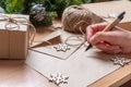 Gift List - Hand holding a pen over a blank sheet of paper, gifts in handmade boxes, snowflakes and fir branches Royalty Free Stock Photo