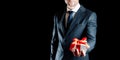 Gift man. Happy young businessman holding surprise gift box present with red ribbon isolated on black background. Black Royalty Free Stock Photo